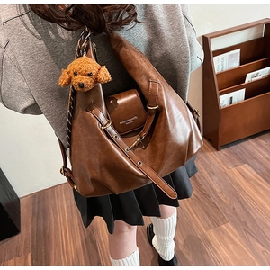 Close-up of brown faux leather tote bag with a plush dog charm on a gray sweatshirt