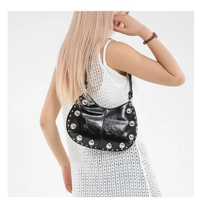 Detail of a black crescent hobo bag featuring large silver rivets and glossy leather texture