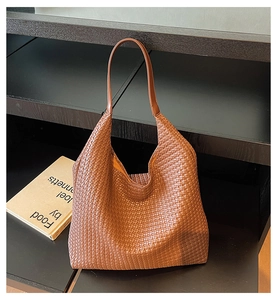 Close-up of caramel brown woven leather Hobo bag displayed on a dark luxury shelf