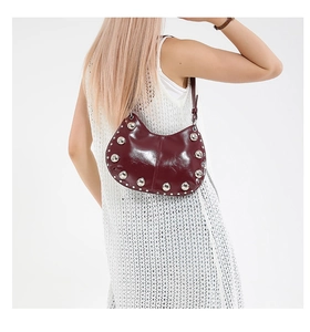 Close-up of burgundy patent leather crescent bag featuring silver metallic rivet studs