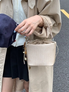 Chic beige woven bucket bag with drawstring closure and wooden bead charm on a model