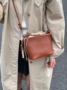 Brown woven drawstring bucket bag with leather strap and wooden bead charm on a model