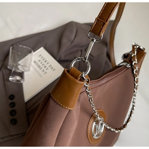 Detail of brown tote bag featuring silver chain and metal M logo on textured fabric