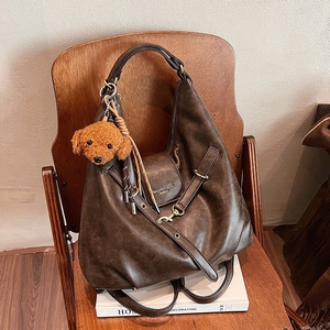 Vintage brown leather tote bag with a cute plush charm displayed on a wooden chair