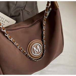 Detail of the brown textured bag showing silver M logo and metal chain strap