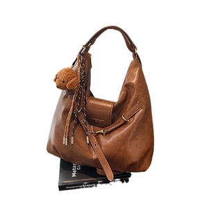 Brown vintage faux leather tote bag with unique handle and teddy bear charm on white background