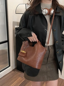 Vintage brown leather tote bag with dual handles and mini charm worn by a model