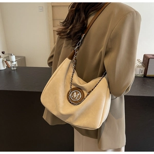 Detail view of the silver M logo and metal chain on a beige suede tote bag for women