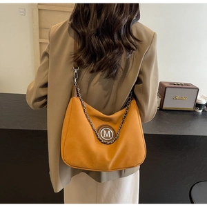 Side view of model wearing an orange suede-textured shoulder bag with a metal M logo