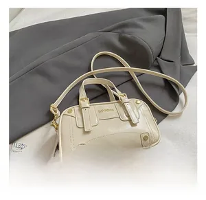 Detail view of cream white glossy leather crossbody bag with gold metal studs and buckle
