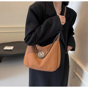 Close-up of caramel leather shoulder bag with metallic M logo and silver chain detail