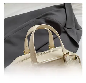 Detail of cream Boston bag featuring cylindrical handles and gold hardware accents
