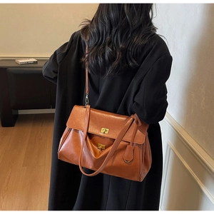 Brown faux leather tote bag with gold swivel lock shown on shoulder with black coat