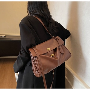 Close-up of brown leather tote bag showing golden square buckles and textured leather finish