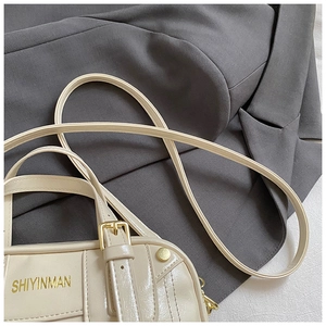 Detail of cream-white handbag with gold buckles and logo on a grey suit background