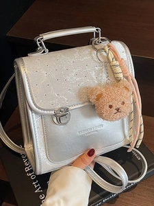 Silver pearlescent backpack with metal buckle and teddy bear charm on black books