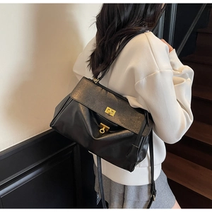 Detail of black faux leather tote bag with gold rectangular turn-lock and side strap buckle