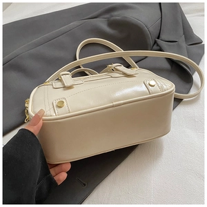 Detail of off-white leather pillow bag featuring golden rivets and handle attachments