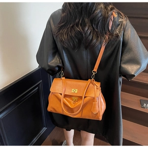 Detail of an amber tote bag with gold swivel lock and adjustable strap on stairs