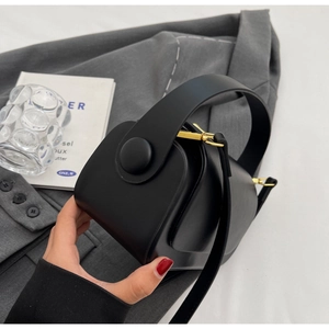 Detail of black matte leather bag with large round button and gold metal hardware