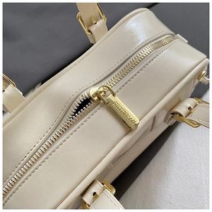 Detailed close-up of cream leather bag with gold-tone zipper and engraved brand logo