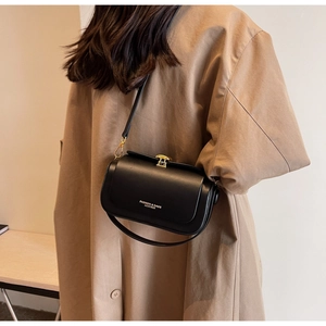 Close-up of black leather rectangular shoulder bag with gold metal buckle and lettering
