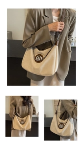 Detail of beige canvas tote bag with brown leather trim and metallic M logo accent