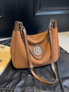 Brown faux suede hobo bag with silver M logo and chain strap on leather background