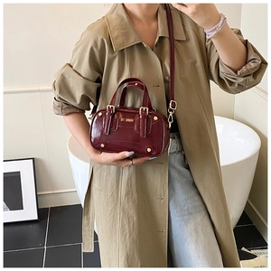 Detailed view of dark red Boston bag with shiny leather and gold hardware