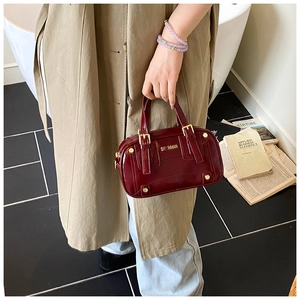 Detail of burgundy patent leather handbag with glossy mirror finish and gold metal accents