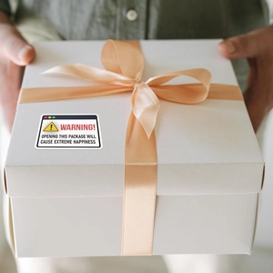 Warning sticker on a white ribbon gift box saying opening will cause extreme happiness
