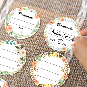 Macro shot of a hand writing on round floral labels for homemade jam jars