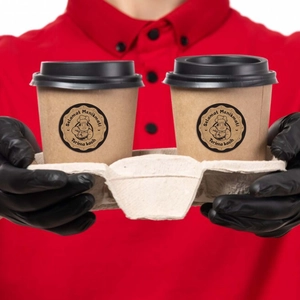 Close-up of kraft coffee cups in a carrier with Selamat Menikmati stickers held by hands