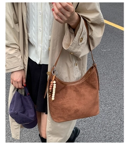 Outdoor lifestyle shot of a retro brown suede shoulder bag featuring a decorative bead charm
