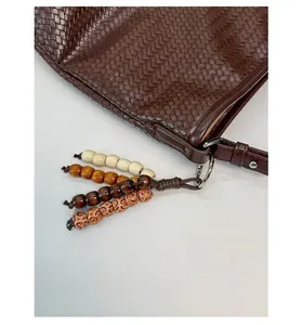 Detail of dark brown woven leather bucket bag featuring decorative wooden bead tassels