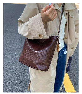 Detail of dark brown woven bucket bag featuring vintage wood bead charm and leather strap