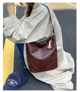 Detail of deep brown woven bucket bag with colorful wood bead tassel on a beige trench coat