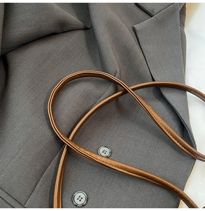 Gros plan des bandoulières en cuir marron et du blazer gris en sergé avec boutons