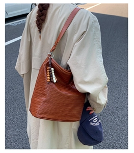 Detail of a brown woven hobo bag featuring a leather strap and wooden bead tassel charms