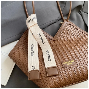 Detail of brown woven faux leather tote bag featuring branded cream ribbons and embossed logo