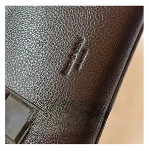 Close-up of deep brown lychee grain leather with embossed brand logo and luxury texture