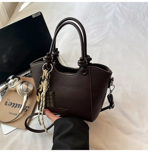 Detail of dark brown litchi pattern leather tote with knot handles and chain charms