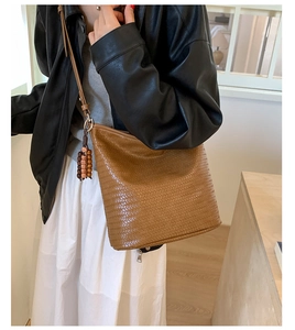 Close-up of brown woven leather bucket bag with wooden bead charm and metallic zipper