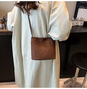 Détail macro du sac seau en daim marron mat avec fine bandoulière sur le mannequin