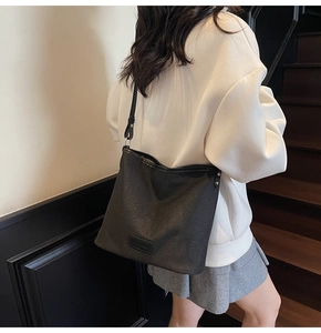 Dettaglio della trama della borsa tote in tela nera portata a spalla da modella