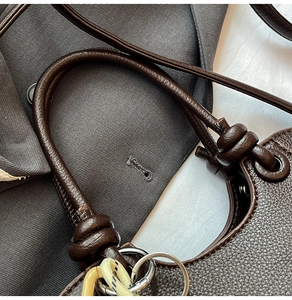 Detail of brown litchi pattern bucket bag showing metal ring and woven rope accessory