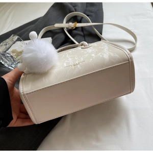 Détail du sac seau crème montrant le panneau texture marbre et le pompon blanc doux