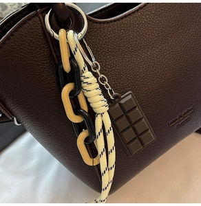 Close-up of dark brown lychee leather bag with designer chains and embossed text details