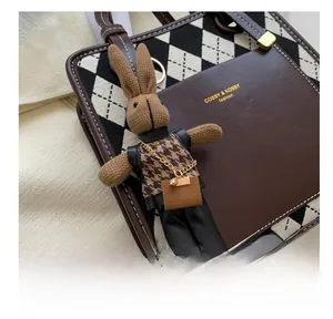 Close-up of a cute rabbit charm on a stylish brown leather and checkered pattern handbag