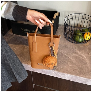Détail du sac seau en cuir marron avec un pendentif chien en peluche et étiquette London